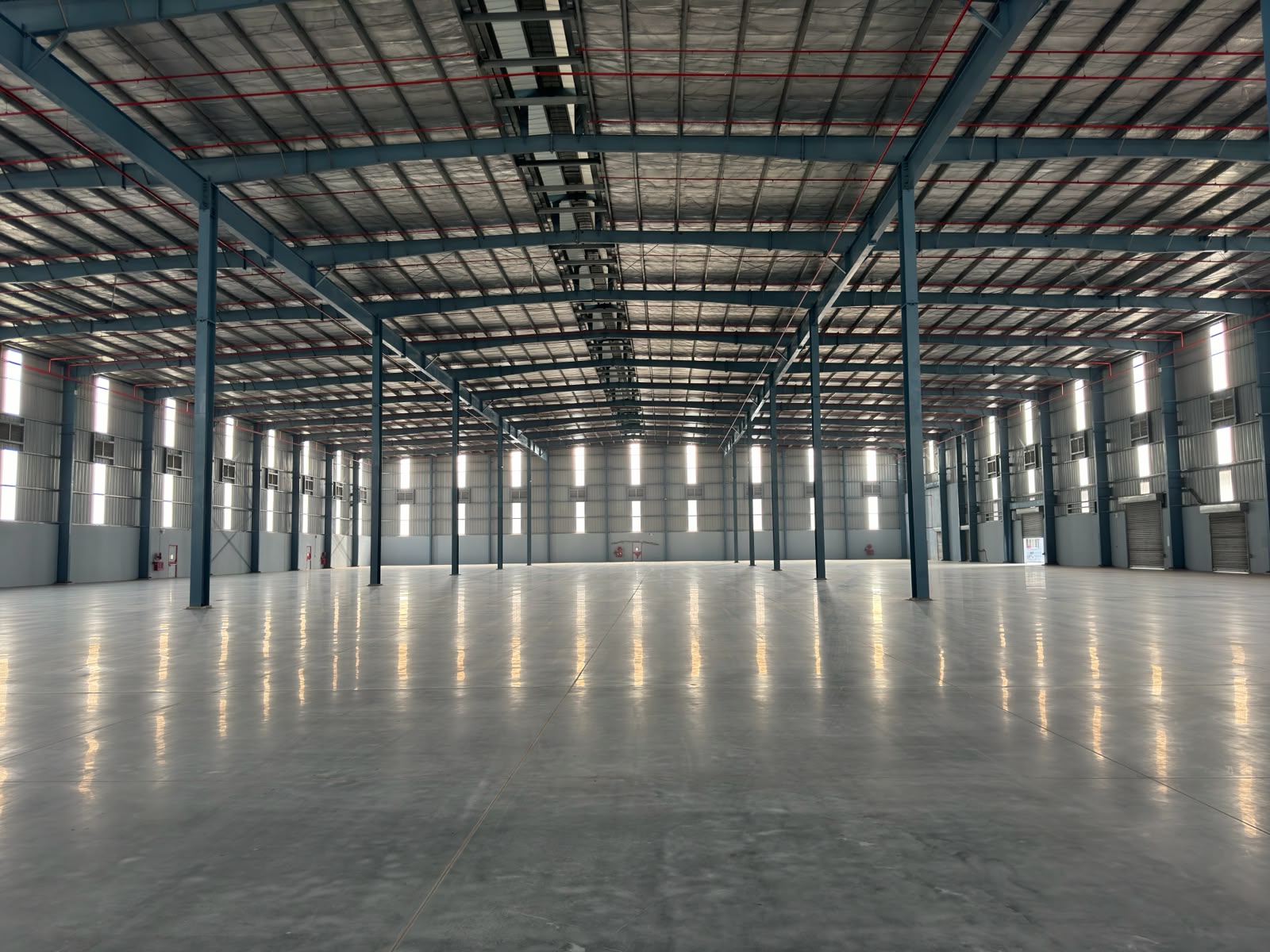 The wide, column-lined interior of a newly completed Grade-A warehouse with a clear-span insulated roof and a polished concrete floor.