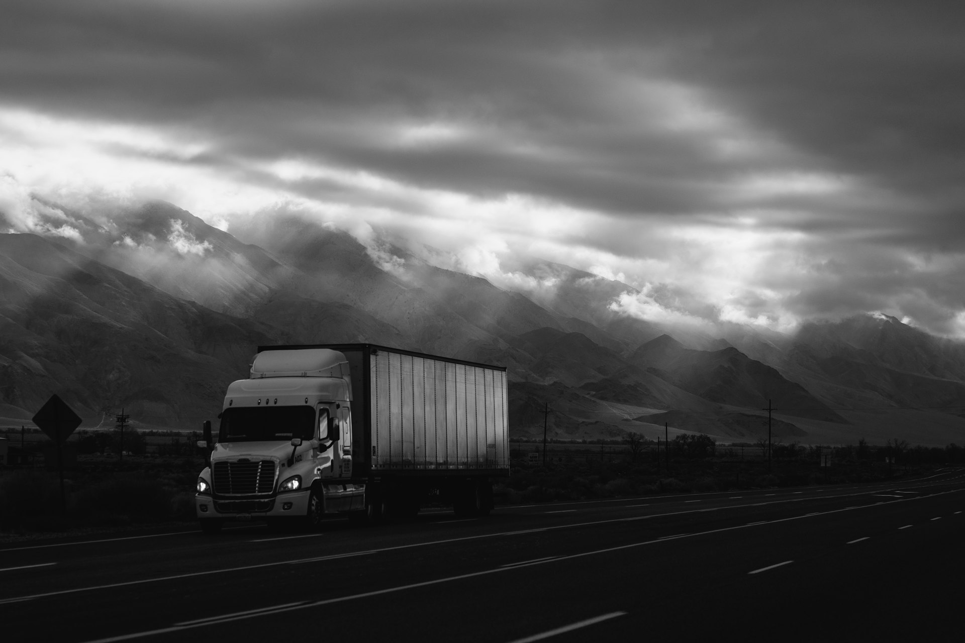 Freight trucks moving along a highway corridor under a dramatic sky.